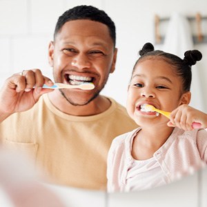 Father and daughter smiling while brushing their teeth