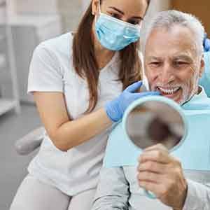 A man admiring his new dental implants with a hand mirror