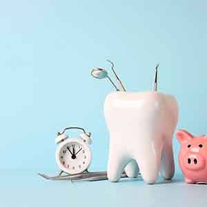 A tooth model with medical instruments, piggy bank and alarm clock on a blue background